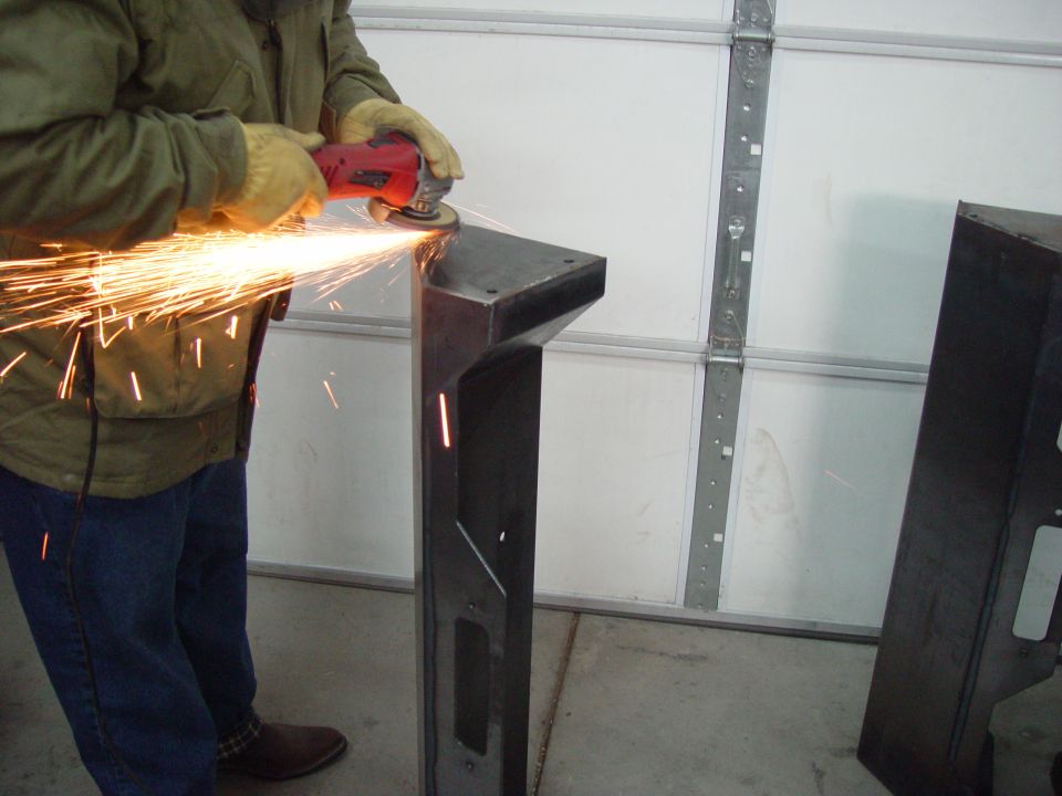 Person wearing gloves and jacket uses angle grinder on a metal component, creating sparks