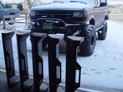1993 Ford Bronco - A lifted Ford Bronco sits in the snow next to a set of four metal brackets.