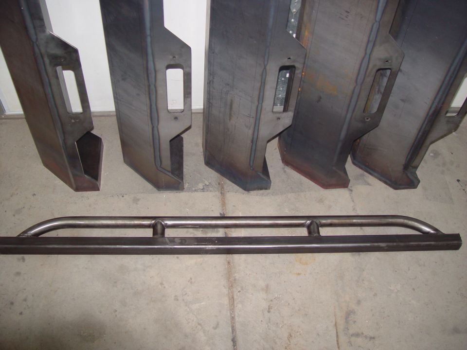 several custom steel bumpers and a set of rock sliders laid out on a concrete floor