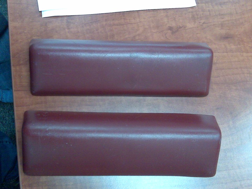Two maroon vinyl armrest pads resting on a wood surface