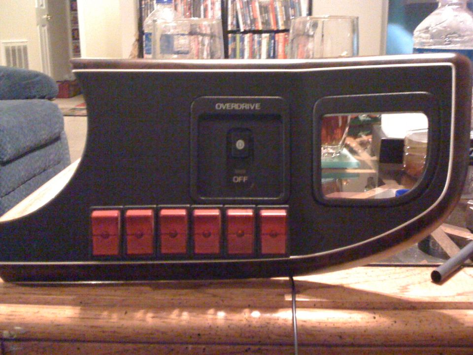 Removed dash trim panel with OVERDRIVE OFF switch and six red rocker switches, shown indoors on a table.