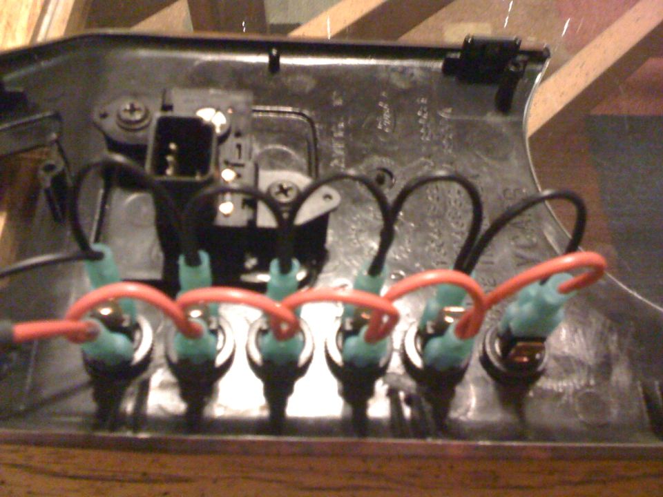 Rear of black switch panel with six switches daisy-chained by red and black wires with green connectors