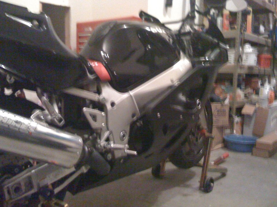 Black Suzuki GSX-R sport bike on a rear stand in a garage with fairings removed, exposing frame and exhaust