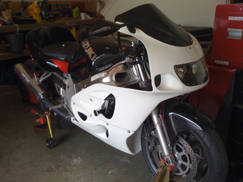 White and black Suzuki sportbike on a rear stand in a garage, front three-quarter view
