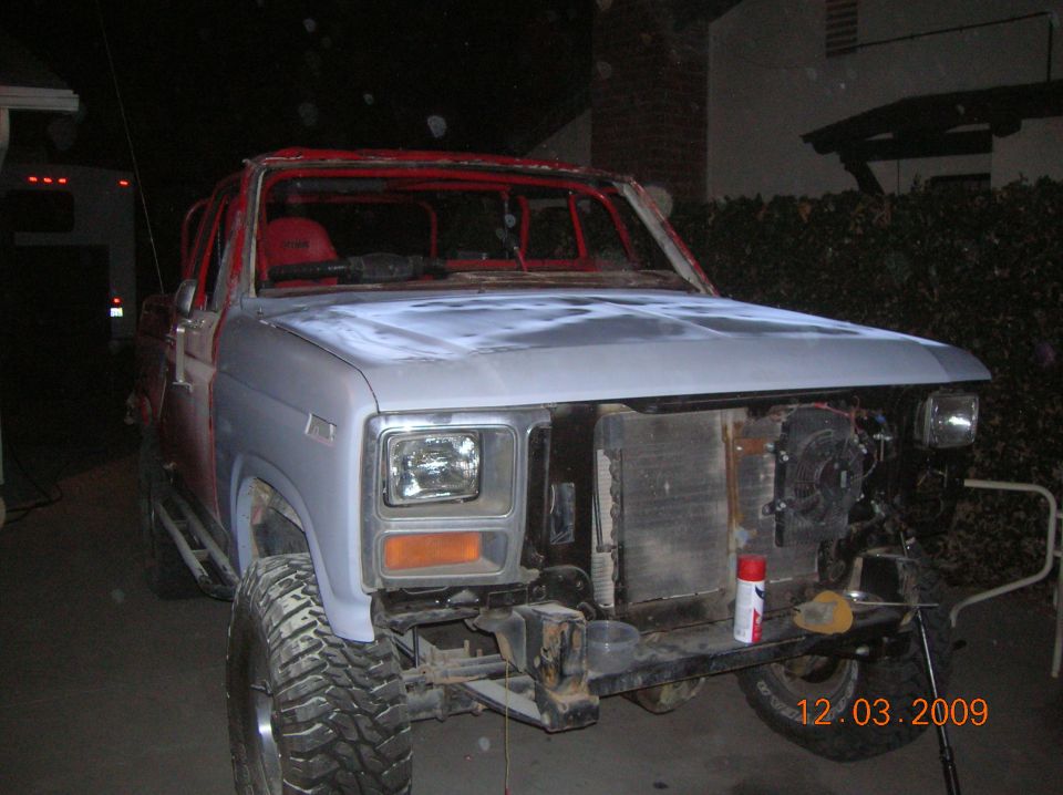 Ford Bronco in primer, front end disassembled, red roll cage visible