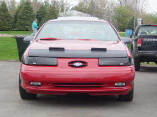 1993 Ford Taurus - A red Ford Taurus is parked outside, with a black pickup truck visible to the right.