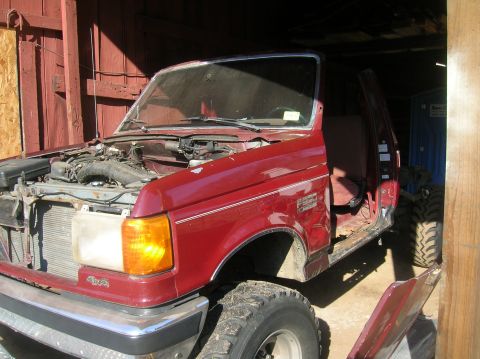 1996 Ford Bronco - This red pickup truck is missing its hood and driver's side door, revealing its engine and interior.