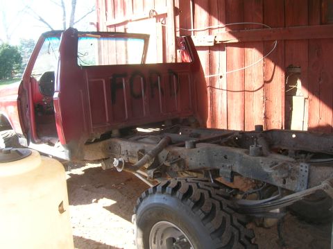 1996 Ford Bronco - The chassis of a red Ford truck, with the word "FORD" spray-painted on the cab back, is shown in a barn.