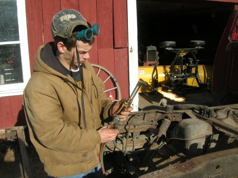 1996 Ford Bronco - Man uses a welding torch on a vehicle frame, with a snowplow in the background.