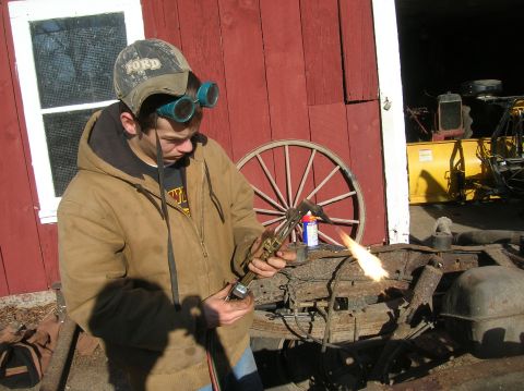 1996 Ford Bronco - A person uses a cutting torch on a rusty metal frame in front of a red barn.