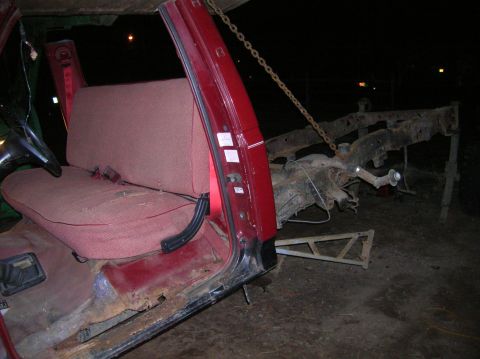 1996 Ford Bronco - The interior of a red vehicle shows significant wear and rust on the chassis, with a chain attached to the frame.