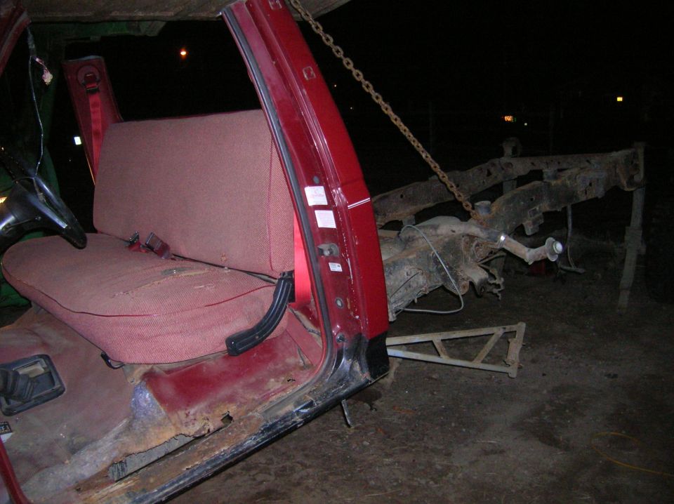 Red vehicle interior with worn seat and exposed chassis. A chain is attached to the frame