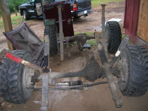 1996 Ford Bronco - The chassis and suspension system of a vehicle, large tires and off-road shocks, with a truck visible in the background.