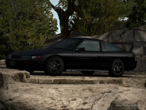 2000 Mercury Grand Marquis - A black sports coupe with a prominent rear spoiler is shown in a side profile against a backdrop of trees and rocks.