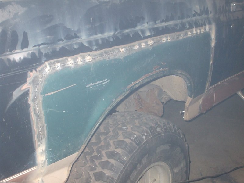 Welded-in teal patch panel on a truck rear quarter during rust repair