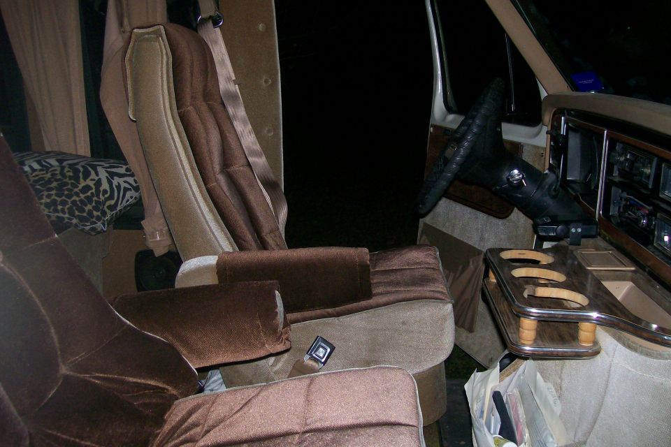 Brown velour captain's chairs and woodgrain cup-holder console in van interior at night
