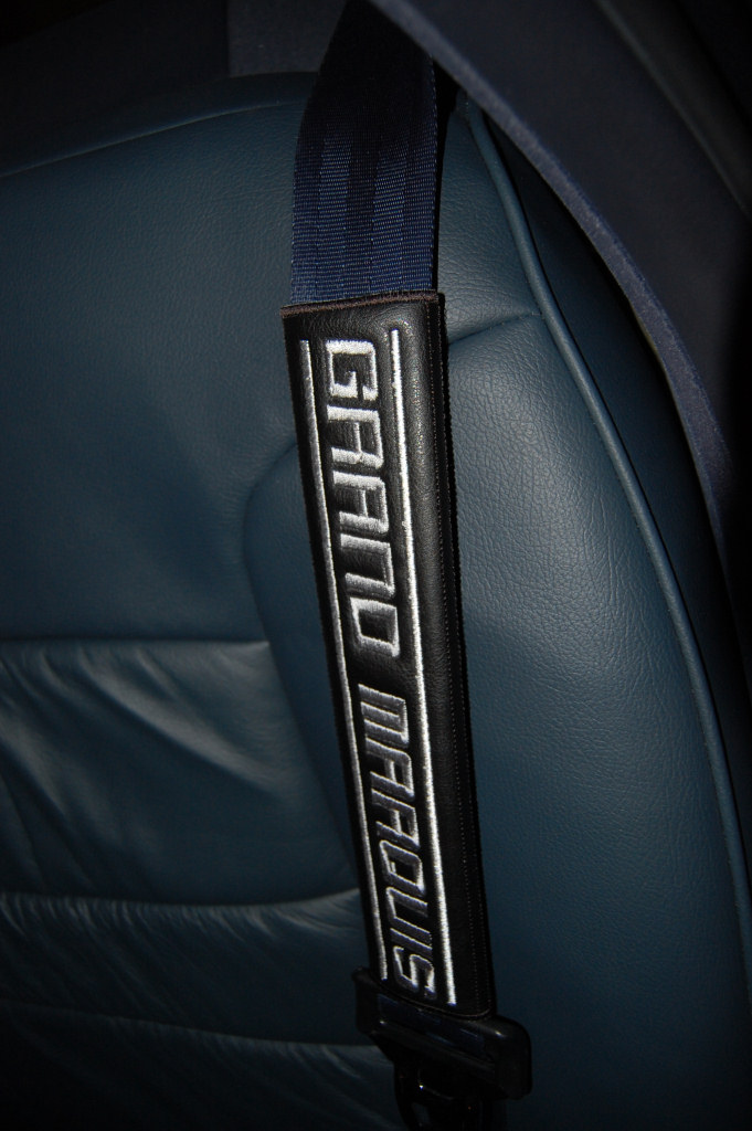 Black seat belt shoulder pad with embroidered white text 'GRAND MARQUIS'