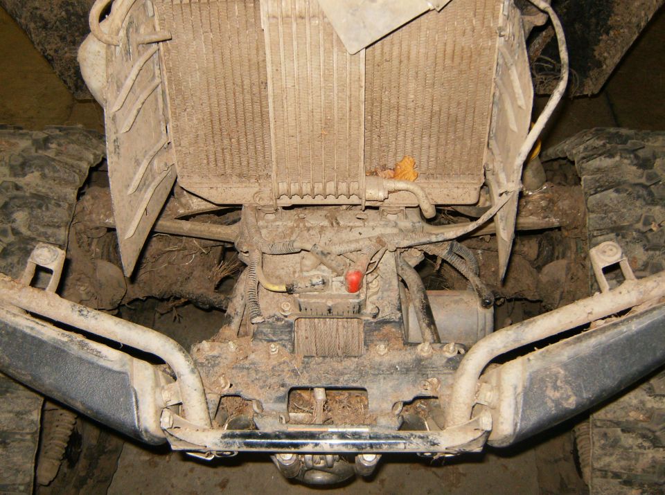 Undercarriage view showing radiator, winch, and front bumper assembly of a heavily soiled vehicle