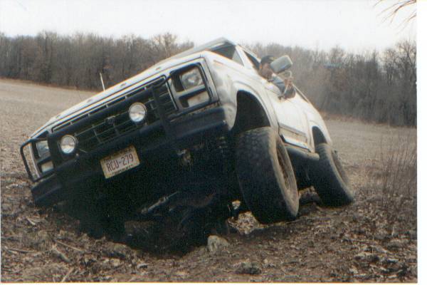 Lifted Ford pickup with grille guard nose-down in a muddy field rut