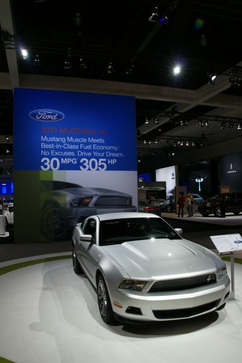 1993 Ford Taurus - 2011 Ford Mustang V6 displayed with promotional signage at an auto show.