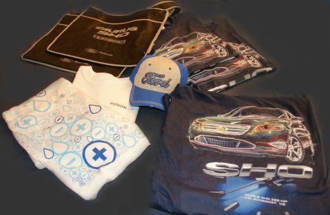 1993 Ford Taurus - Various Ford Taurus SHO branded merchandise including t-shirts, a hat, and a bag are arranged on a dark surface.