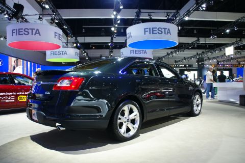 1993 Ford Taurus - A dark sedan is displayed at an auto show with 'Fiesta' banners overhead.