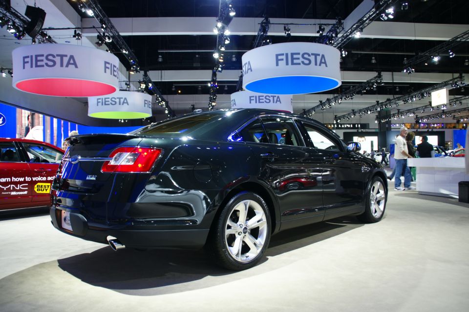 Dark sedan with a spoiler and chrome wheels at an auto show