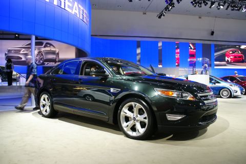 1993 Ford Taurus - A dark green sedan is displayed at an auto show, with other vehicles visible in the background.