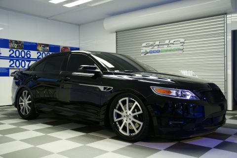 1993 Ford Taurus - Black sedan with custom wheels in a showroom setting, a timeline on the wall.