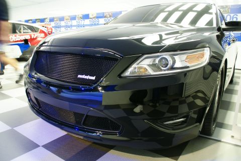 1993 Ford Taurus - A black car with a custom grille and modern headlights is displayed indoors.