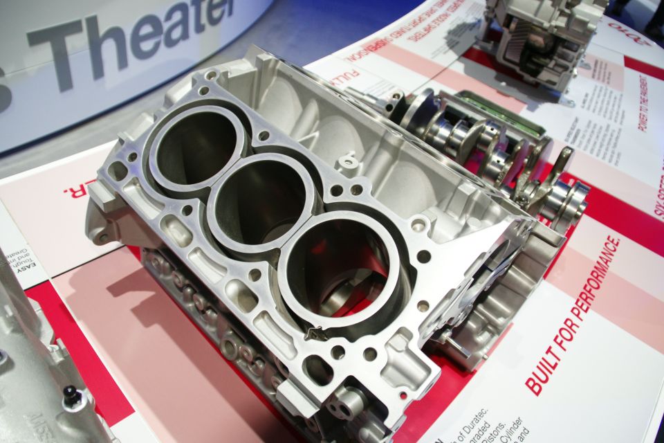 Cutaway engine block with three cylinders visible, alongside a crankshaft and other engine components