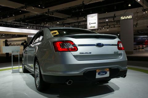 1993 Ford Taurus - A silver Ford Taurus is displayed at an auto show with other brand signage in the background.