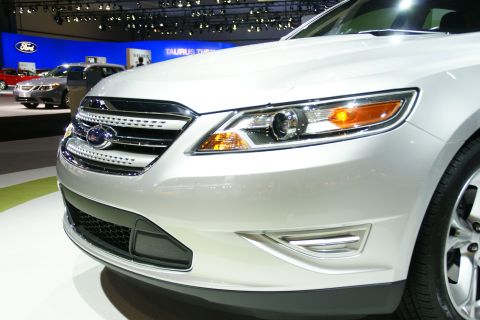 1993 Ford Taurus - A white Ford sedan is displayed at an auto show, with other vehicles visible in the background.