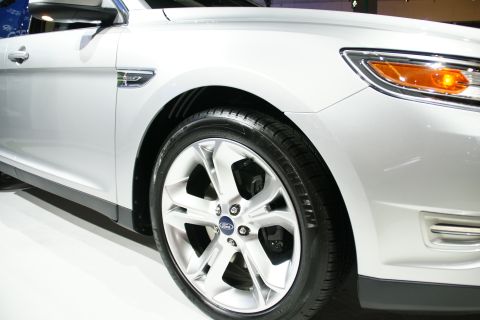 1993 Ford Taurus - The front quarter panel and wheel of a silver sedan are visible, with a Ford emblem on the wheel hub.