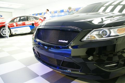 1993 Ford Taurus - A black sedan is displayed indoors with a racing car in the background.