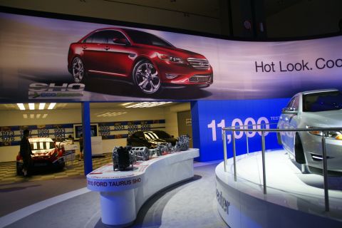 1993 Ford Taurus - A display at an auto show features a red Ford Taurus SHO on a banner and a silver Ford Taurus on a pedestal.
