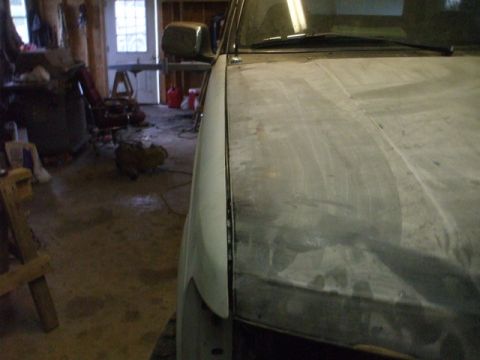 1995 Ford Bronco - Close-up view of a vehicle's hood and fender, showing an unfinished surface in a garage setting.