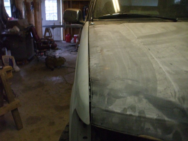Sanded truck hood and fender in primer inside a garage during bodywork