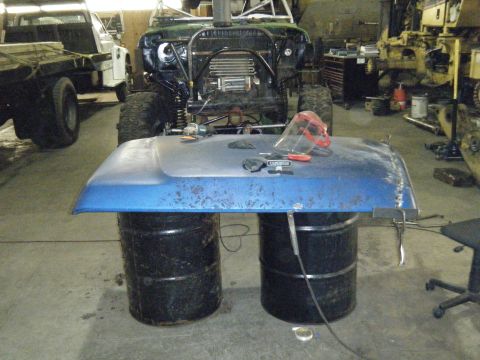 1978 Ford Bronco - A workshop scene shows a heavily modified off-road vehicle with a blue hood placed on barrels in front of it.
