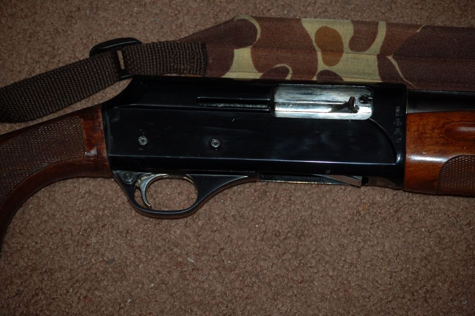 Blued shotgun receiver, trigger, and wood stock on carpet