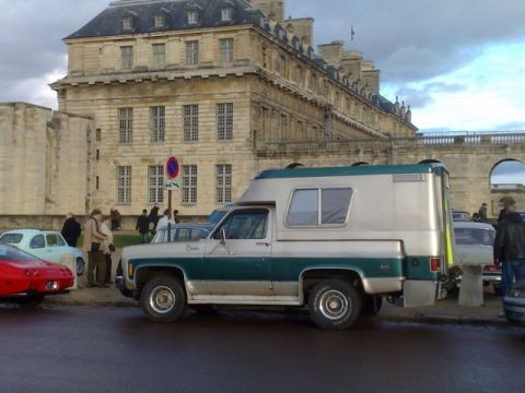 1991 Ford Crown Victoria - Two-tone Chevrolet/GMC pickup truck with camper shell parked near a historic building.