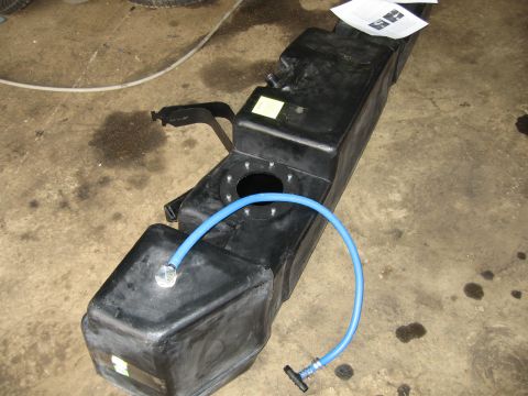 2005 Dodge 3500 - A black plastic fuel tank with a blue hose connected to a cap sits on a concrete floor.