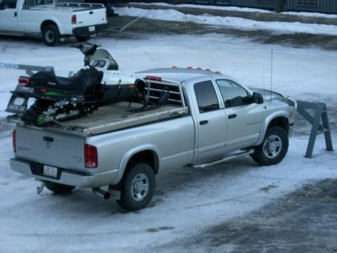2005 Dodge 3500 - A silver 2005 Dodge 3500 pickup truck is parked in the snow, with a snowmobile loaded in its bed. Another white pickup truck is visible in…