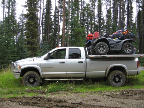 2005 Dodge 3500 - Silver Dodge 3500 pickup truck carrying an ATV and gear, parked in a wooded area.