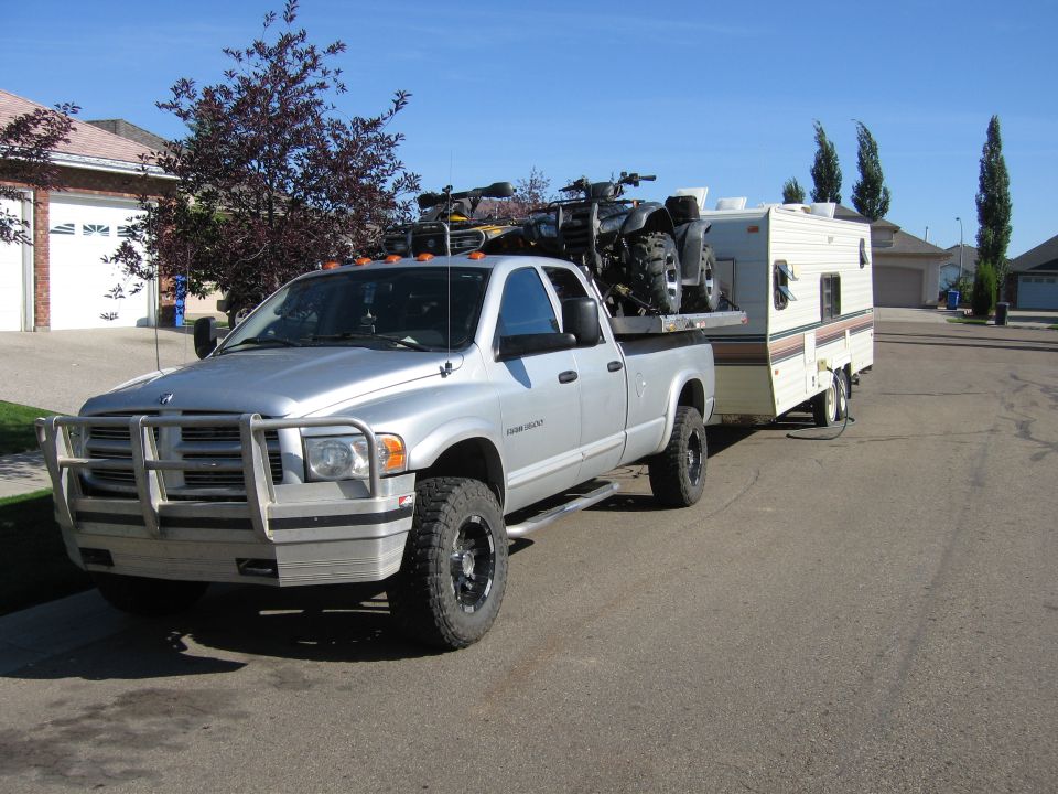 Silver 2005 Dodge 3500 towing a trailer with ATVs on a flatbed