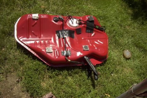 1997 Ford Taurus - A red fuel tank with attached hoses and wiring is shown on a grassy surface.