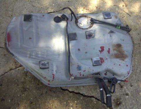1997 Ford Taurus - A detached fuel tank is shown from above, resting on a cracked concrete surface.