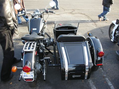 1998 Ford Crown Victoria - A black motorcycle with a sidecar is parked outdoors, with people walking in the background. The license plate is visible.