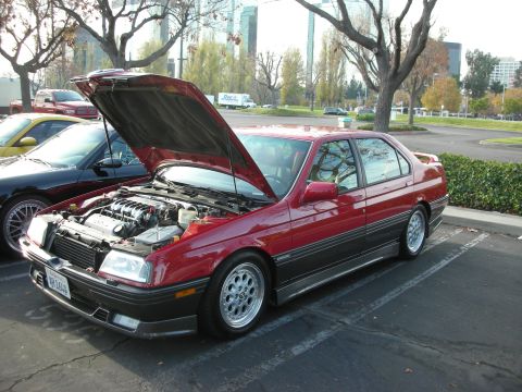 1998 Ford Crown Victoria - A red sedan with its hood open, revealing a V6 engine, is parked in a lot next to another vehicle.
