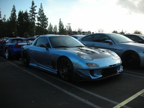 1998 Ford Crown Victoria - A blue Mazda RX-7 is parked in a lot with other vehicles.